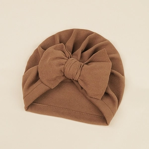Detailed view of caramel brown baby turban hat with oversized knit bow on beige background