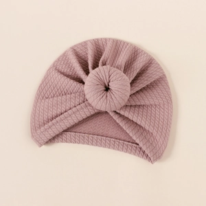 Close-up of mauve waffle knit baby donut hat with decorative knot on soft background