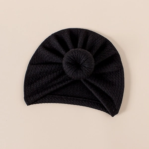 Detail of black ribbed knit baby turban hat with a round donut knot on beige background