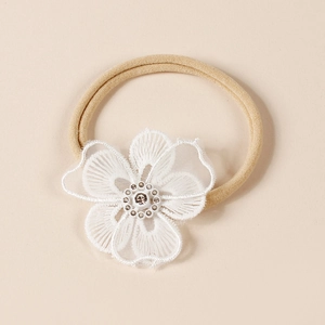 Détail de la fleur en dentelle brodée blanche sur un bandeau bébé en nylon souple beige