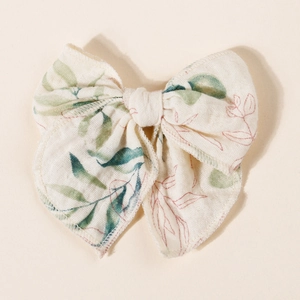 Detailed view of beige muslin fabric bow hair clip with green leaf and brown branch patterns