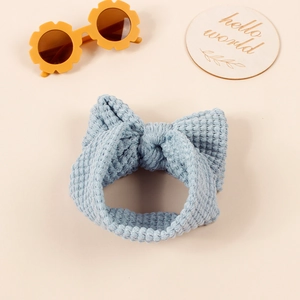 Light blue waffle knit baby headband with a large bow on a soft beige background