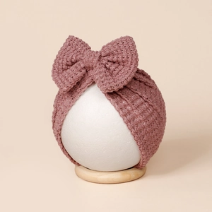 Détail du bonnet turban pour bébé en tricot avec texture gaufre et grand nœud sur mannequin