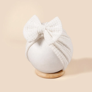 Gros plan du bonnet turban blanc en tricot pour bébé avec grand nœud décoratif