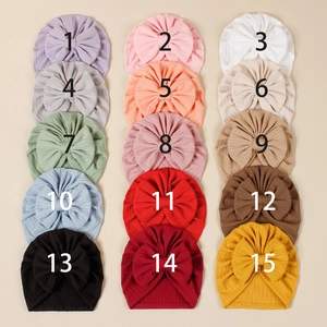 Flat lay display of 15 colorful stretch knit baby beanies with bow details in 3x5 matrix
