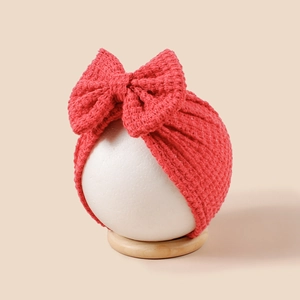 Gros plan du bonnet turban rouge tricoté à la main pour bébé avec un grand nœud doux