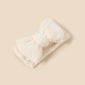 Detail of cream knitted baby headband showing the soft waffle texture and large double bow