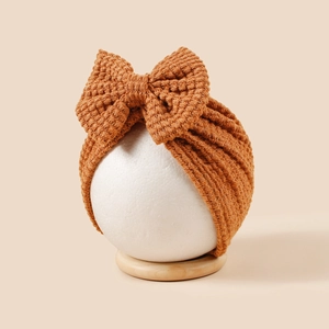 Gros plan d'un turban en maille caramel pour bébé avec nœud géant sur un support