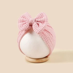 Détail d'un bandeau en tricot rose pour bébé avec un grand nœud décoratif sur mannequin