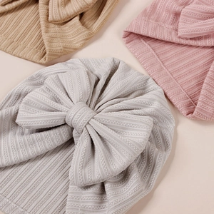 Detailed view of three soft ribbed knit baby beanies with large bows in grey pink and beige