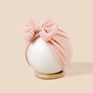 Gros plan d'un turban tricoté rose pour bébé orné d'un grand nœud sur fond neutre