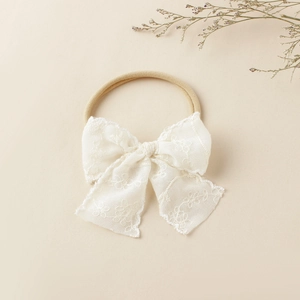 Détail d'un bandeau pour bébé avec nœud en dentelle blanche brodée et ruban élastique doux