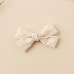 Detail of cream lace bow hair clip with embroidered hollow patterns and scalloped edges