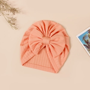 Close-up of soft peach baby beanie featuring rib-knit texture and large bow detail