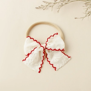 Détail du bandeau bébé avec nœud en dentelle blanche, bord rouge et ruban nylon élastique