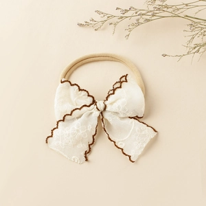 Gros plan du bandeau en dentelle blanche pour bébé avec des bords brodés marron