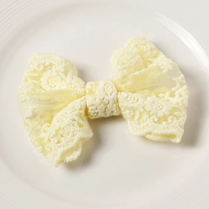Detailed macro view of a cream yellow lace bow hair clip with floral embroidery patterns