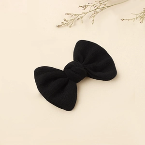 Close-up of black knitted bow hair clip featuring soft fabric texture on a beige background