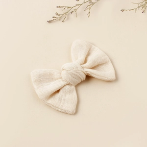 Close-up of off-white cotton fabric bow clip showing natural coarse woven texture