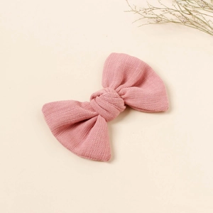 Detail view of a pink bow hair clip with textured fabric on a warm beige background