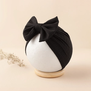 Detail of baby black ribbed knit headband with large bow on wooden display stand