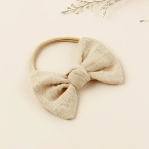 Close-up of a beige cotton baby headband with a soft bow and elastic nylon band