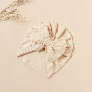 Detail of baby turban hat featuring ribbed knit texture and a large soft bow in cream