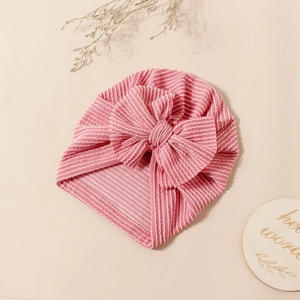 Detail of pink striped baby turban hat with bow knot and texture on wooden background