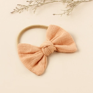 Close-up of beige cotton linen baby bow headband with soft elastic nylon band and fabric texture