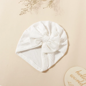 Detailed texture of white ribbed baby turban hat with a bow on cream background