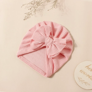 Detailed view of pink striped baby turban hat with a large bow on warm background