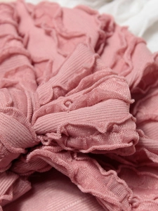 Dettaglio ravvicinato di tessuto a balze rosa e trama orizzontale su un cappello neonato