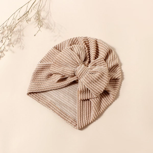 Detail of baby striped turban hat with a large bow on a soft neutral background
