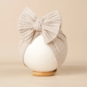 Détail d'un bonnet bébé beige en maille gaufrée avec un grand nœud décoratif