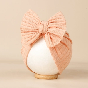 Détail d'un bonnet en maille gaufrée pour bébé avec un grand nœud sur support en bois
