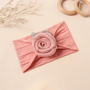 Detail eines rosa gestrickten Babystirnbands mit großer 3D-Stoffrose und Silberblättern