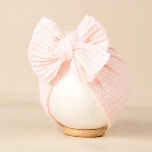 Détail du bonnet pour bébé en maille gaufrée rose clair avec un grand nœud décoratif