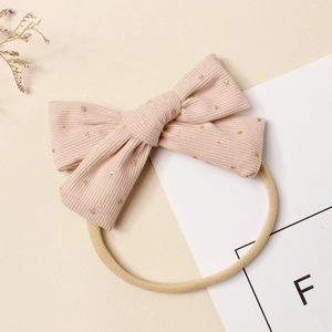 Vue détaillée du nœud en velours côtelé rose avec paillettes dorées sur bandeau bébé