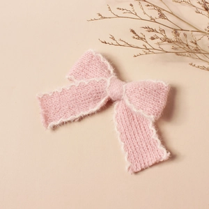 Dettaglio molletta per capelli a fiocco rosa in maglia con bordo bianco e lana morbida