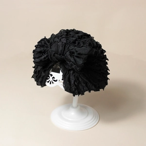 Dettaglio cappello a turbante nero plissettato per neonati con fiocco su supporto