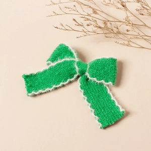 Dettaglio del fermaglio per capelli a fiocco in maglia verde con bordo in finta pelliccia