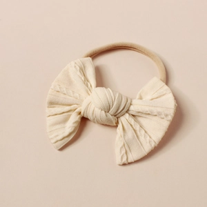 Nahaufnahme des cremeweißen Strick-Stirnbands für Babys mit weichem Zopfmuster und Schleife