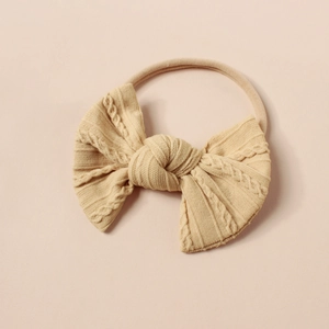 Nahaufnahme des beigen gestrickten Zopfmuster-Stirnbands für Babys mit elastischem Band