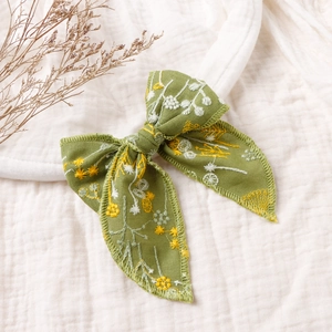 Detail of green linen hair bow with yellow floral embroidery on white cotton fabric