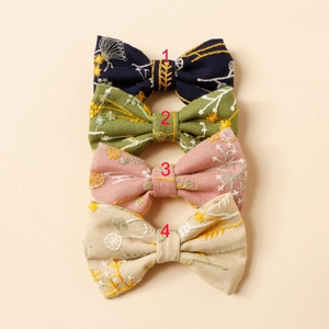 Détail de quatre barrettes nœuds brodées de fleurs en marine, vert, rose et beige
