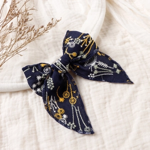 Detail of navy blue embroidered floral bow hair clip on a textured white fabric background