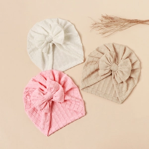 Detailed texture of baby turban hats with large bows in white, pink, and beige colors