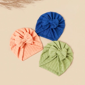 Detailed flat lay of three ribbed baby turban hats in navy blue, coral, and light green hues