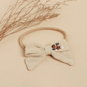 Détail du bandeau bébé avec nœud en coton et broderie florale en ton beige chaud