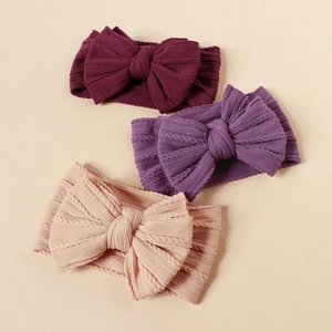 Detailed view of three elastic knitted baby headbands with large bows in varied colors